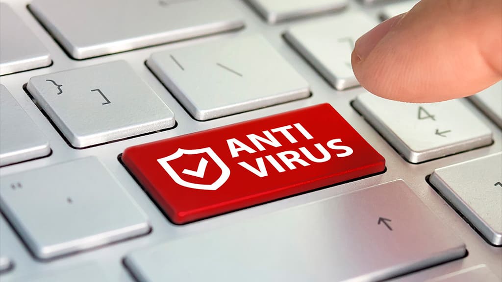 Teclado de um computador na cor branca. Em destaque, uma tecla em vermelhor escrito "Antivírus" e um dedo em direção a esta tecla.