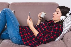 Uma mulher deitada o sofá, tomando café e ouvindo um audiobook do aplicativo do Skeelo.