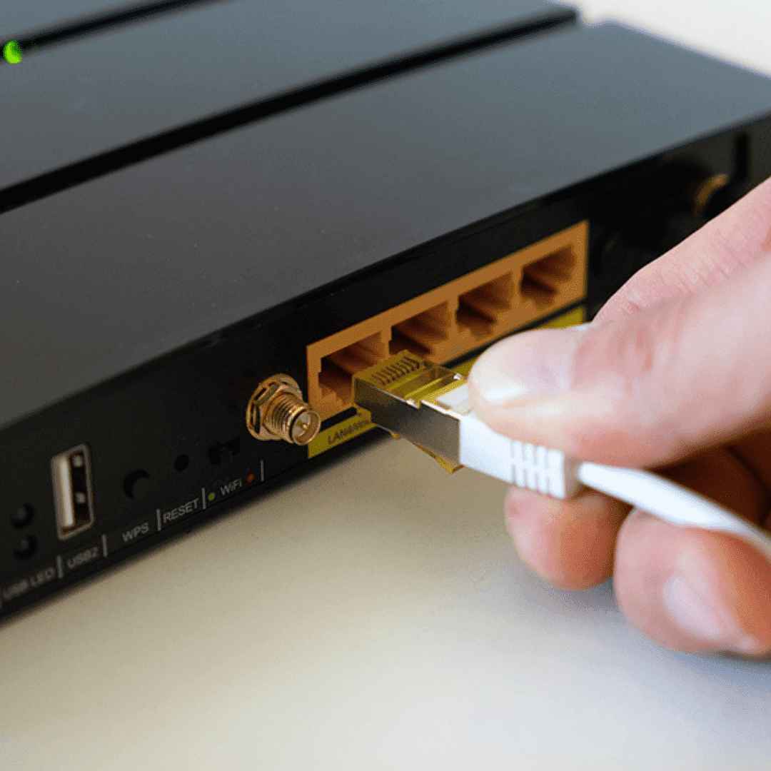 Um modem na cor preta e uma mão, segurando um cabo branco, direcionando o cabo para ser conectado.