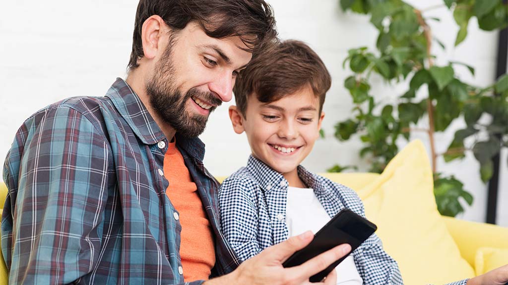 Pai e filho lendo no celular. Eles usam o aplicativo do Skeelo.