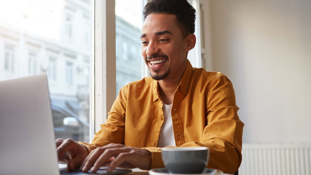 Um homem, com o semblante feliz, usando o notebook. Ele está solicitando o "Desbloqueio em confiança" no site da Desktop Internet.